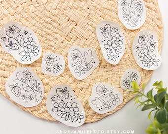 Puede incluir: Una colección de nueve pegatinas blancas con ilustraciones de líneas negras que muestran fresas, flores y hojas. Cada pegatina tiene una forma orgánica irregular. El texto SHOPJAMIEPHOTO.ETSY.COM está impreso en la parte inferior.
