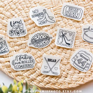 May include: A collection of nine white stickers with black line art designs featuring hockey themes, text including 'hockey boys', 'BRIAR HOCKEY', 'puck me, baby', 'I f*cking love ROLLER COASTERS', 'BRIAR', 'GRAHAM 44', 'Malone', 'line!', and 'NO! BERNARDO! HOW?' with various icons.