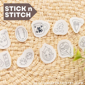 May include: A set of ten iron-on patches featuring characters and objects from the popular animated film, "My Neighbor Totoro." The patches are white with black outlines and are arranged on a woven straw background. The text "STICK n STITCH" is visible at the top of the image.