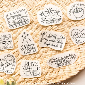 May include: A collection of nine white stickers with black line art and text including phrases like enemies to lovers, Romantasy Reader, Cauldron Boil Me, Chapter 55, Night Court, stay with the high lord, Smut, shadow daddy, Rhys Would Never, and Bat Boys.