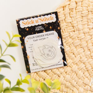 May include: A black and gold card with the text "Stick n'Stitch" and "Your order means the world". The card has a white sticker with a black and white illustration of a fire creature with a smiling face.
