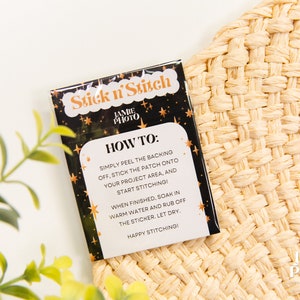 May include: A black and gold card with the text "Stick n' Stitch" and instructions on how to use the product. The card is on a woven straw surface.