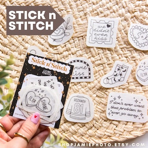 May include: A collection of Stick n' Stitch patches with various designs, including hearts, socks, and a jersey. The patches are black and white and are displayed on a woven surface. The text "STICK n STITCH" is at the top.