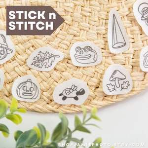 Puede incluir: Un conjunto de 10 parches termoadhesivos con varios diseños lindos, que incluyen un hongo, una calabaza, una rana, una hoja, una tortuga, una linterna, una bruja, una roca, un cono y una tetera. Los parches son blancos y tienen contornos negros. El texto "STICK n STITCH" está escrito en marrón sobre un fondo blanco.