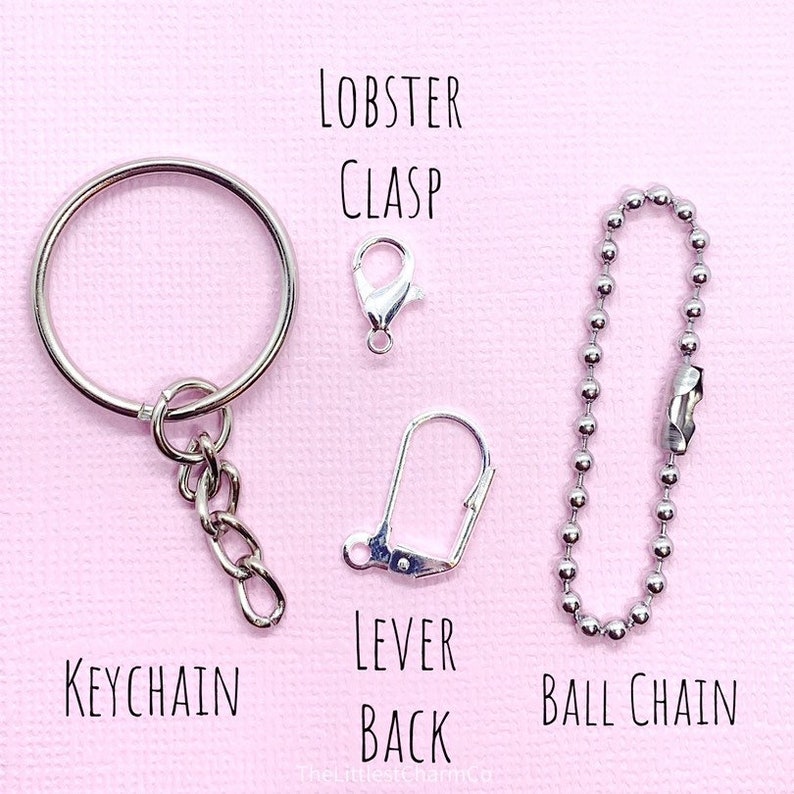 May include: A collection of silver-colored keychain hardware, including a keychain ring, lobster clasp, lever back, and ball chain. The text labels each item: KEYCHAIN, LOBSTER CLASP, LEVER BACK, and BALL CHAIN. The background is a soft pink.