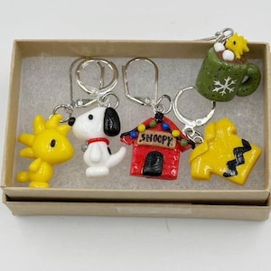 Puede incluir: Un conjunto de cinco llaveros de personajes con Snoopy y sus amigos. Los llaveros incluyen un Woodstock amarillo, Snoopy, la caseta de Snoopy, una taza verde con un copo de nieve y un Charlie Brown amarillo. Los llaveros están en una pequeña caja de cartón.