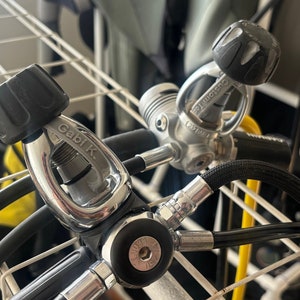 May include: Two silver scuba diving regulators with black hoses and black knobs. The regulator on the left has the text "Gabi K" on it.