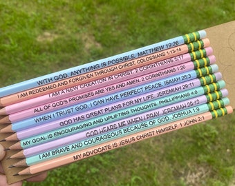 May include: A set of ten colorful pencils with inspirational quotes and bible verses printed on them. The pencils are arranged in a stack with the tips facing up. The quotes include: "With God, anything is possible", "I am redeemed and forgiven through Christ", "I am a new creation in Christ", "All of God's promises are yes and amen", "When I trust God, I can have perfect peace", "God has great plans for my life", "God hears me when I pray", "My goal is encouraging and uplifting thoughts", "I am brave and courageous because of God", and "My advocate is Jesus Christ himself".