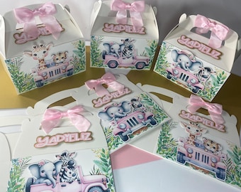 May include: Pink and white favor boxes with a jungle animal theme. Each box features a different animal, including a giraffe, zebra, and elephant, riding in a pink jeep. The boxes are decorated with green leaves and the name "YADYELLZ" is written on each box.