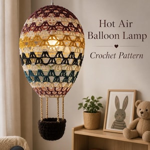 May include: A hanging hot air balloon lamp featuring a multi-colored crochet pattern in shades of maroon, yellow, black, and teal. The balloon is suspended above a dark brown crocheted basket. The text reads Hot Air Balloon Lamp Crochet Pattern.