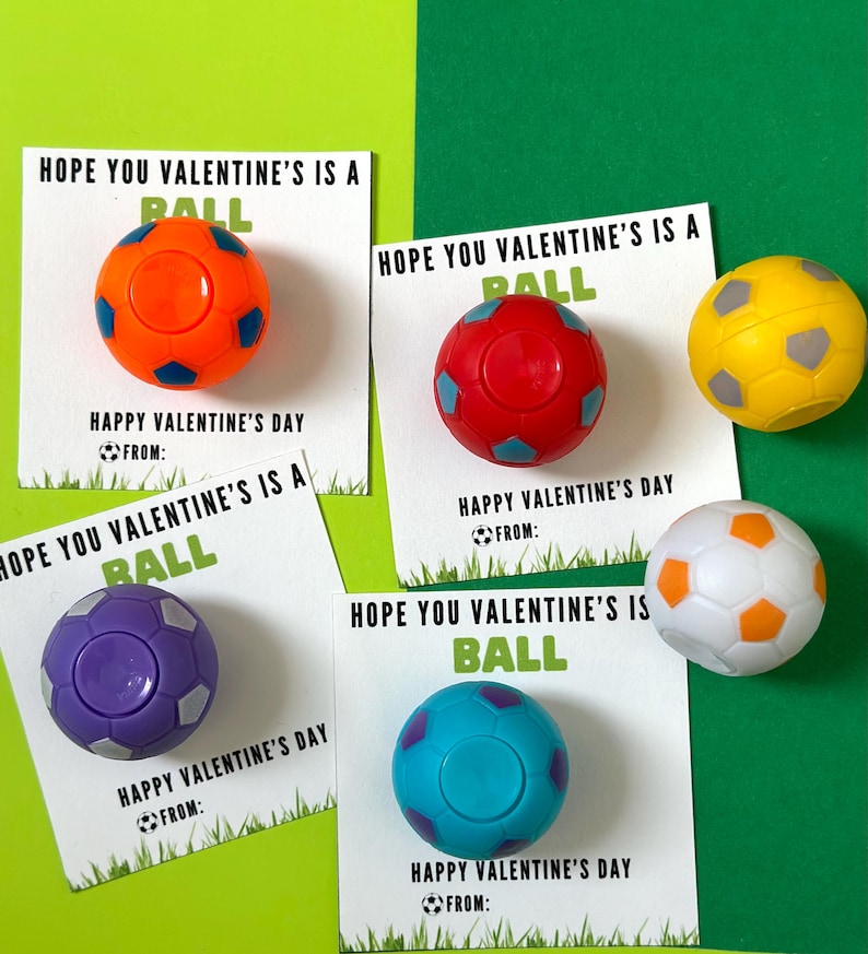 May include: Four Valentine's Day cards with the text "Hope you Valentine's is a ball" and a small soccer ball attached to each card. The soccer balls are orange, red, purple, and blue.