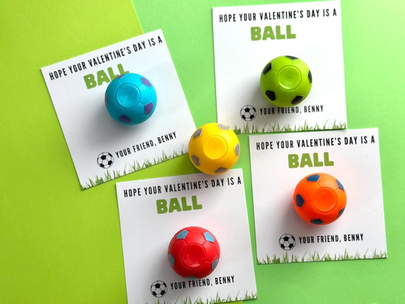May include: Four Valentine's Day cards with the message "Hope your Valentine's Day is a BALL" and a small soccer ball attached to each card. The soccer balls are blue, green, yellow, and orange.