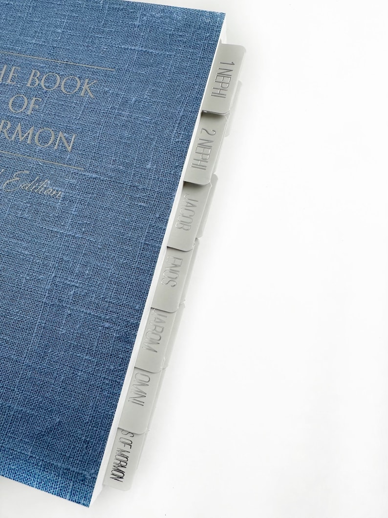May include: A blue book with the title "The Book of Mormon" and a set of gray tabs labeled with the names of the books in the book, including 1 Nephi, 2 Nephi, Jacob, Jarom, Omni, and Words of Mormon.