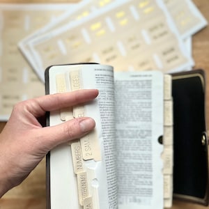 May include: A close-up of a white leather-bound Bible with beige tabs labeled with the names of books of the Bible, including Joshua, Deuteronomy, Numbers, 2 Samuel, Judges, and Genesis.