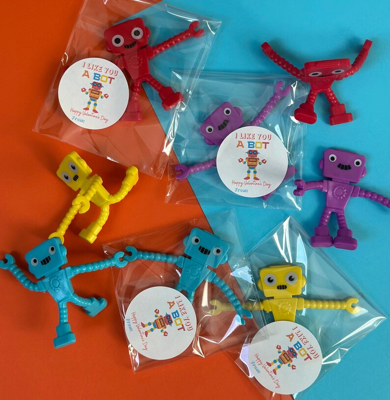 Może przedstawiać: Sześć małych plastikowych zabawek robot&oacute;w zapakowanych w przezroczyste plastikowe torebki z naklejkami walentynkowymi, na kt&oacute;rych widnieje napis "I Like You A Bot" i "Happy Valentine's Day".