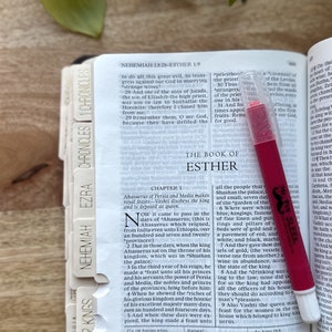 May include: Close-up of an open Bible with a pink highlighter on the page. The page is open to the Book of Esther, Chapter 1. The text on the page describes the king's feast and the queen's disobedience.