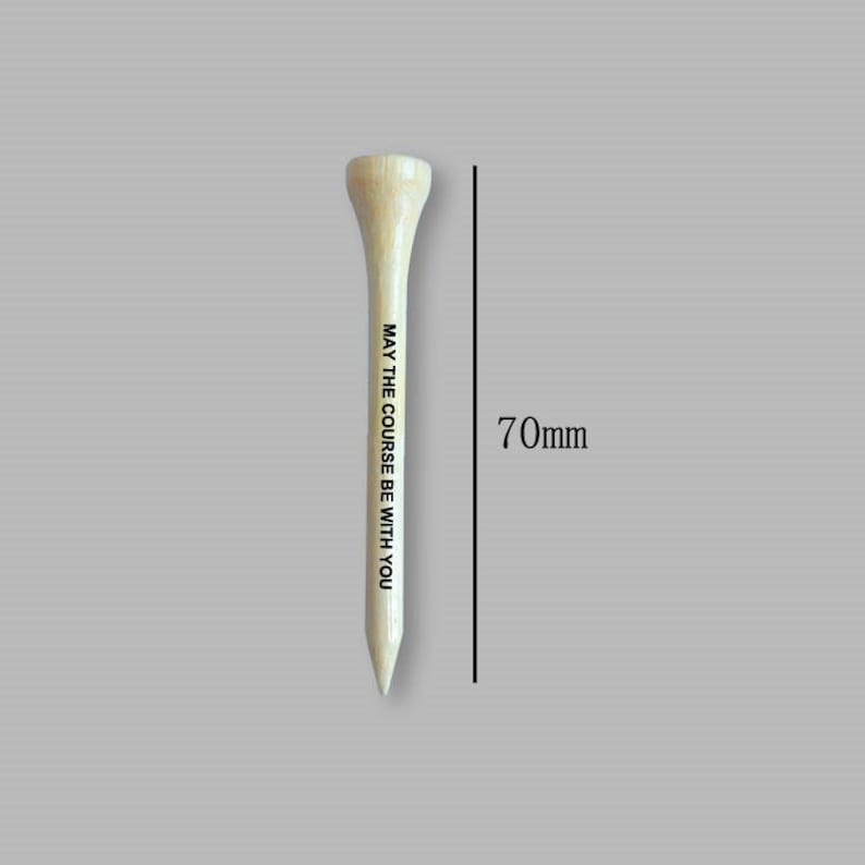 Puede incluir: Un tee de golf de madera, de 70 mm de largo, con el texto "MAY THE COURSE BE WITH YOU" impreso verticalmente. El tee es de color claro con una parte superior redondeada y un extremo puntiagudo, sobre un fondo neutro.