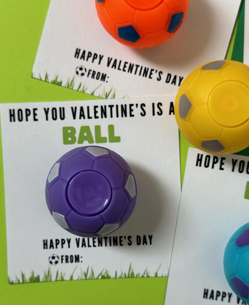 May include: Three Valentine's Day cards with a soccer ball theme. Each card has a different colored soccer ball attached to it. The text on the cards reads "Happy Valentine's Day" and "Hope you Valentine's is a ball".