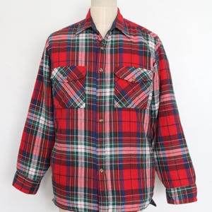 Puede incluir: Una camisa de franela a cuadros rojos, verdes, azules y blancos con dos bolsillos en el pecho. La camisa de manga larga es abotonada y se muestra en un maniquí. La camisa es de estilo clásico.