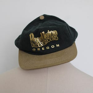 May include: A green and brown baseball cap with the text "Pendleton Underground Oregon" in gold lettering.