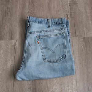 May include: Light blue denim jeans folded neatly. The jeans feature a classic five-pocket design, a button and zipper closure, and the iconic Levi's back pocket stitching. The orange Levi's tag is visible on the back pocket.