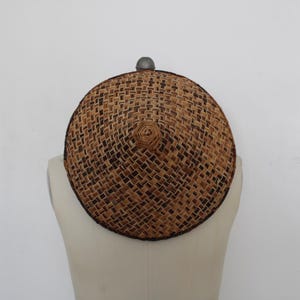 May include: A round, woven hat with a conical crown, displayed on a mannequin. The hat features a tightly woven pattern in shades of brown and tan, with a dark brown border. The hat's diameter is approximately 14 inches.