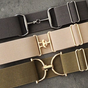 May include: Three elastic belts with different colored fabric and metal buckles. The first belt is black with a silver buckle. The second belt is beige with a gold buckle. The third belt is green with a gold buckle.