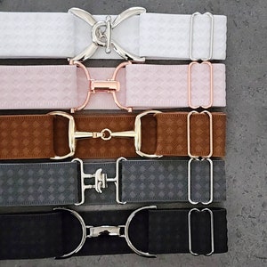 May include: Five elastic belts with different coloured fabrics and metal buckles. The belts have a diamond pattern and are available in white, pink, brown, grey, and black.
