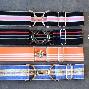 Pode incluir: Quatro cintos el&aacute;sticos de diferentes riscas com fivelas de metal. Os cintos s&atilde;o pretos com riscas cor-de-rosa, pretos com riscas vermelhas e cinzentas, laranja com riscas brancas e azuis com riscas douradas. Os n&uacute;meros 7, 8, 9 e 10 s&atilde;o vis&iacute;veis no lado direito da imagem.