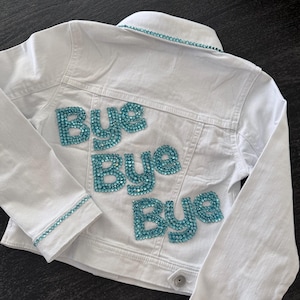 May include: White denim jacket with the words "Bye Bye Bye" spelled out in turquoise rhinestones on the back. The jacket has turquoise rhinestone trim along the collar, cuffs, and pockets.