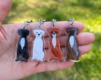 May include: Four clear acrylic keychains featuring different colored boxer dogs. The dogs are black, white, brown, and brindle.