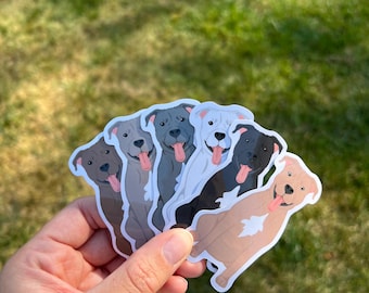 Peut inclure: Cinq autocollants de pit-bulls de dessin animé de différentes couleurs. Les autocollants sont dans une main, et les chiens sourient tous avec la langue tirée.