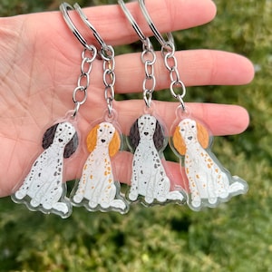May include: Four clear acrylic keychains featuring a cartoon illustration of a white and brown English Setter dog. Each keychain has a silver metal chain and ring.
