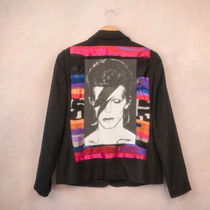 May include: Black blazer with a colorful striped patch on the back featuring a black and white image of David Bowie.