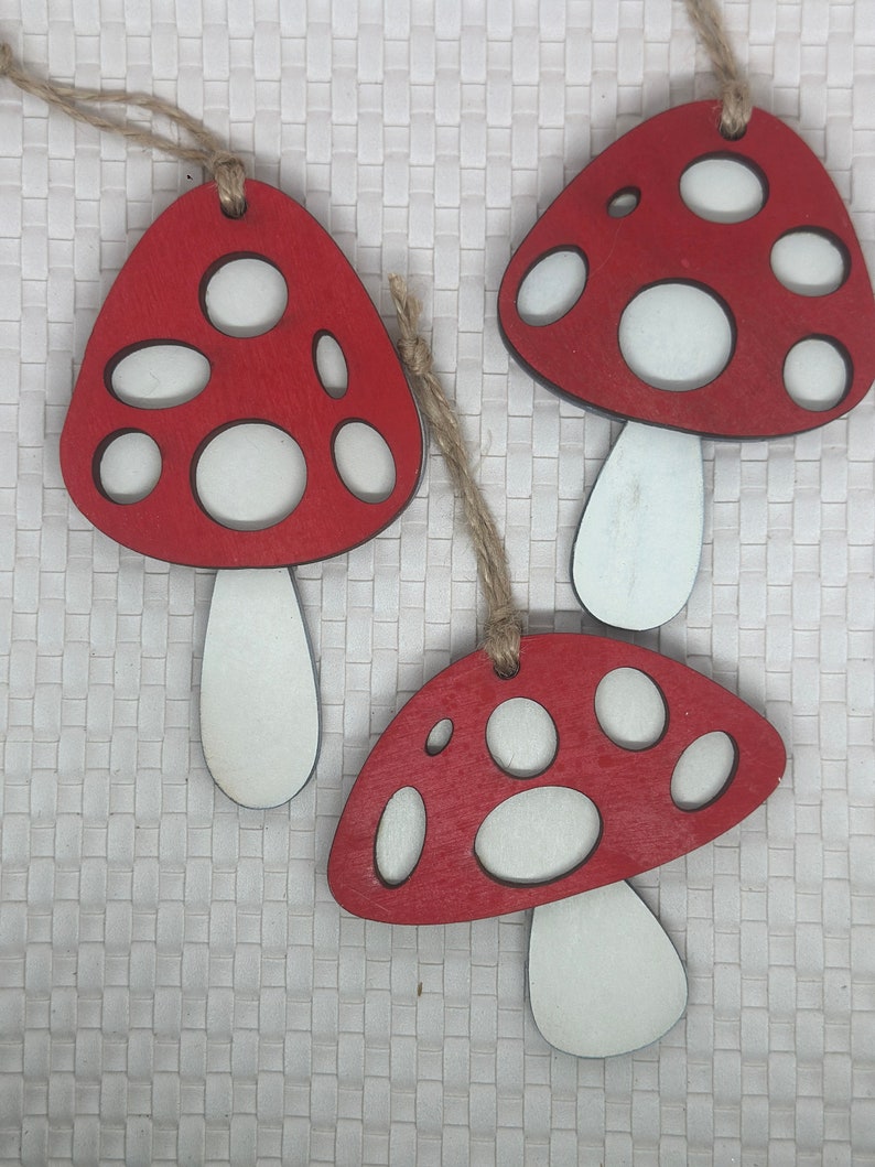 Op de afbeelding: Drie rode en witte houten paddenstoelversieringen met witte stelen. De paddenstoelen hebben een rustieke, handgeschilderde uitstraling.