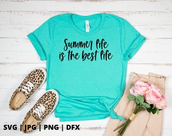 Pode incluir: Uma camiseta azul turquesa com o texto "Summer life is the best life" em letras pretas. A camiseta está sobre um fundo de madeira branca com um buquê de flores cor-de-rosa e sapatos de estampa de leopardo.