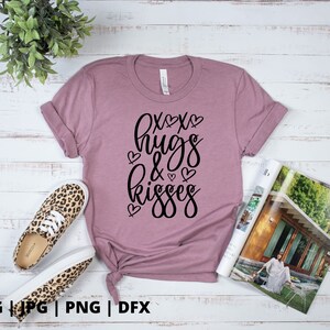 K&ouml;nnte beinhalten: Ein mauvefarbenes T-Shirt mit dem Text "XOXO hugs & kisses" in schwarzer Schrift mit kleinen Herzen um den Text.