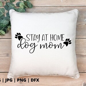 Peut inclure: Un oreiller blanc avec du texte noir qui dit "Stay at Home Dog Mom" avec des empreintes de pattes de chaque c&ocirc;t&eacute; du texte.