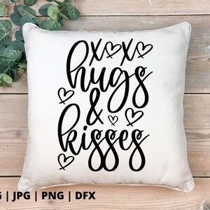 K&ouml;nnte beinhalten: Ein wei&szlig;es Kissen mit schwarzem Text, der "oxox hugs & kisses" lautet, mit kleinen Herzen um den Text herum.