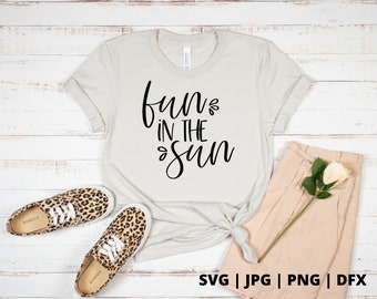 Pode incluir: Uma camiseta branca com o texto "fun in the sun" em letras de escrita preta. A camiseta está colocada sobre um fundo de madeira branca com um par de tênis de estampa de leopardo e shorts bege.