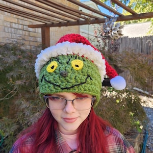 May include: A green crocheted hat with a smiling face, yellow eyes, and a red and white Santa hat on top.