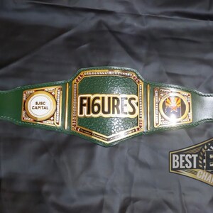 May include: A green leather championship belt with gold accents. The center plate features the word "FIGURES" in gold lettering. The side plates feature the words "S.J.S.C. CAPITAL" and a logo with a star and the text "ZONA". The belt is labeled "BEST B.C.B. BELTS CHAMPIONSHIP".