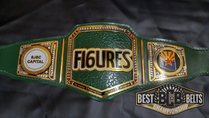 May include: A green wrestling championship belt with gold accents and rhinestones. The belt features the words "FIGURES" in white letters with a gold outline, "SJSC CAPITAL" in white letters on a black circle, and a gold circle with the Arizona state flag. The belt also has the words "Grassroots Champion Arizona 2023" and "BEST BCB BELTS CHAMPIONSHIP" in gold letters.