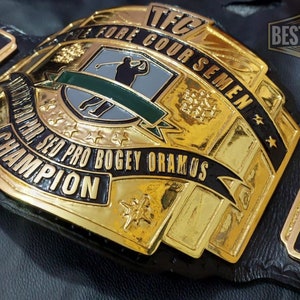 May include: A gold and black championship belt with the text "SED PRO BOGEY ORAMOS CHAMPION" and "TFC FORE COUR SEMEN". The belt features a golf-themed design with a golfer silhouette and the words "BEST B&B BELTS CHAMPIONSHIP".