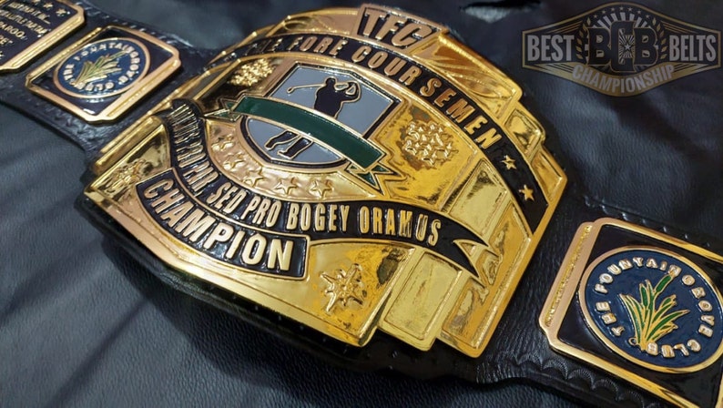 May include: A gold and black championship belt with the text "SED PRO BOGEY ORAMOS CHAMPION" and "TFC FORE COUR SEMEN". The belt features a golf-themed design with a golfer silhouette and the words "BEST B&B BELTS CHAMPIONSHIP".