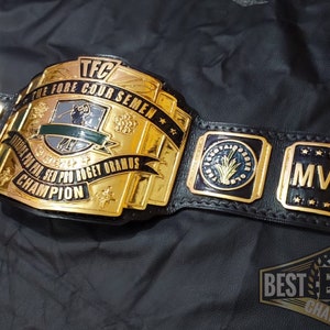 May include: A gold and black championship belt with the text "TFC THE FORE COUR SEMEN" and "CHAMPION". The belt has gold plates with the word "MVP" and other text. The belt is on a black surface.