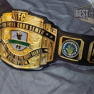 May include: A gold and black championship belt with the text "TFC THE FORE COUR SEMEN" and "STOKES PRO PRO. SED BOGEY ORAMOS CHAMPION". The belt has the text "MVP" and "FOUNTAIN GROVE CLUB" on it.