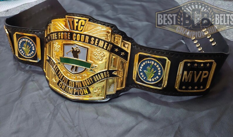 May include: A gold and black championship belt with the text "TFC THE FORE COUR SEMEN" and "STOKES PRO PRO. SED BOGEY ORAMOS CHAMPION". The belt has the text "MVP" and "FOUNTAIN GROVE CLUB" on it.