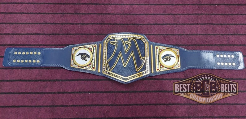 May include: A blue and gold championship belt with a large "M" in the center and a panther logo on each side. The belt is made of leather and has a gold buckle. The text "Morton Panthers" is printed on the belt.