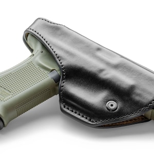 Può includere: Un fodero in pelle nera con chiusura a scatto, progettato per contenere una pistola verde e nera.